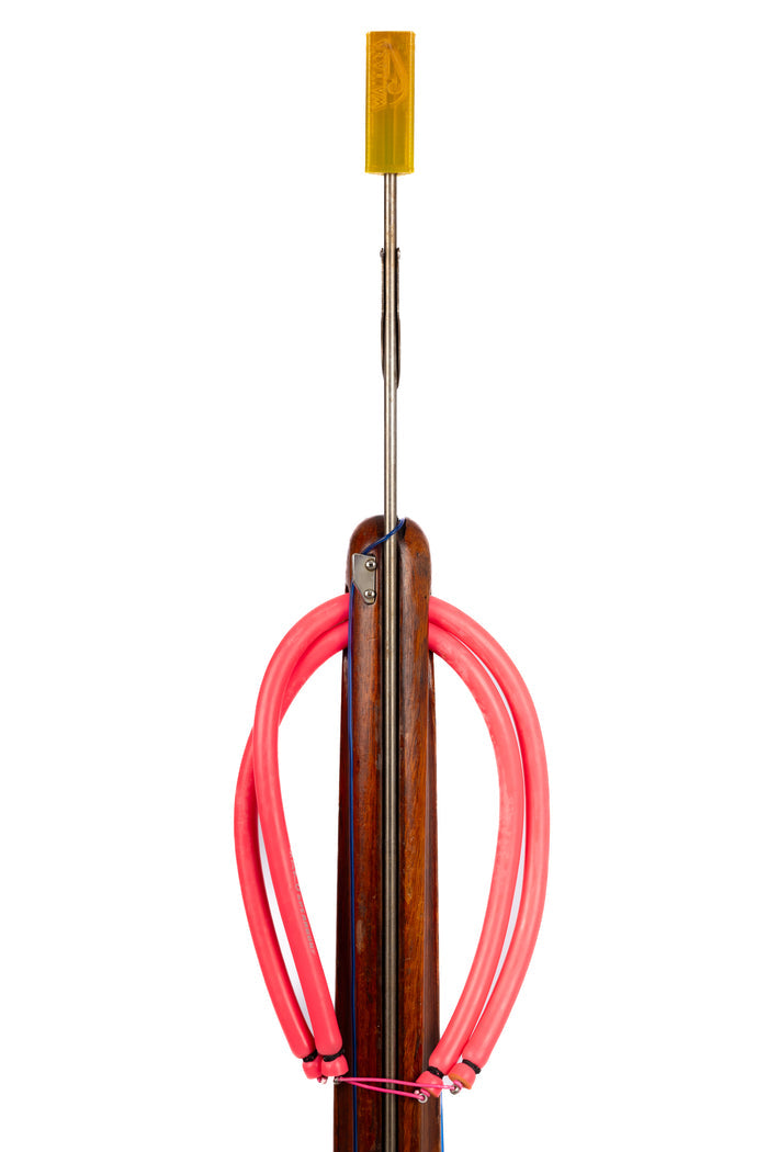 A yellow Waihana flexible spear tip protector fitted onto the stainless steel shaft of a wooden speargun loaded with pink rubber bands, photographed against a white background.