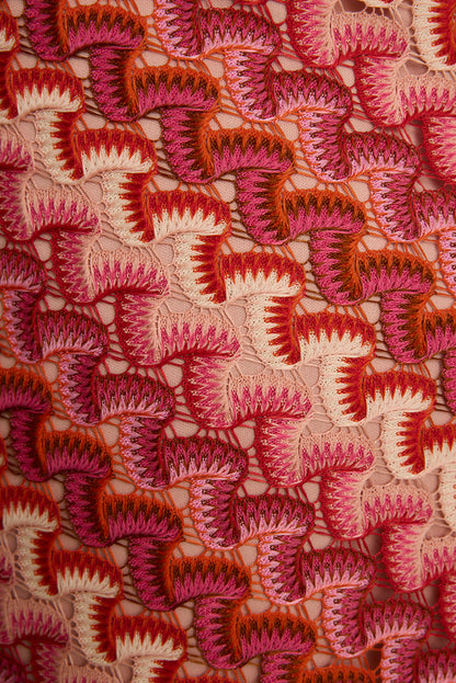 Close-up of pink and orange crochet knit skirt fabric, an open shell-stitch resort look.