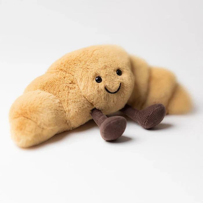 Plush toy shaped like a croissant with a smiling face on a white background
