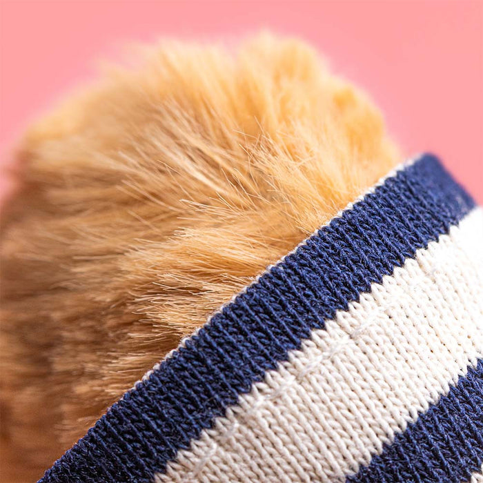 Close-up detail of Jellycat Bartholomew Bear's golden-brown curly fur ear and the navy-and-cream striped knit fabric of the seafarer top, against a pink background