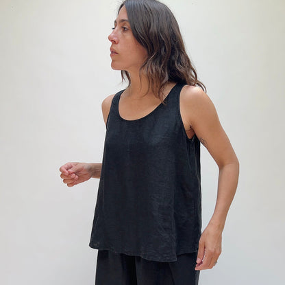 A person with long brown hair wearing a black linen tank top and matching black linen pants.