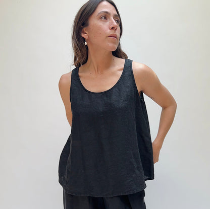 A person looking up and away from the camera with long brown hair wearing a black linen tank top and matching black linen pants.