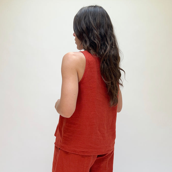 A person turned away from the camera wearing a red linen tank top and matching pants, standing against a plain background.