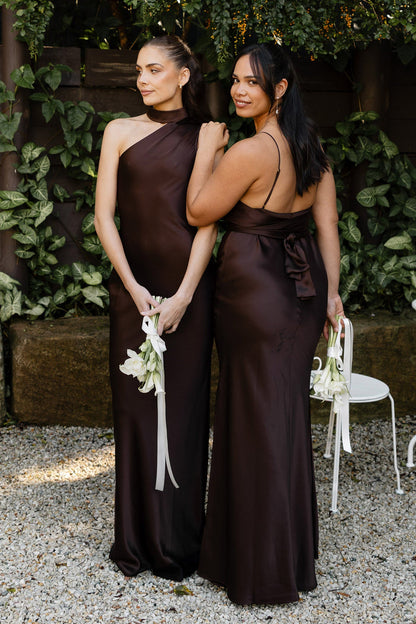 Two women in brown bridesmaid dresses in a garden setting