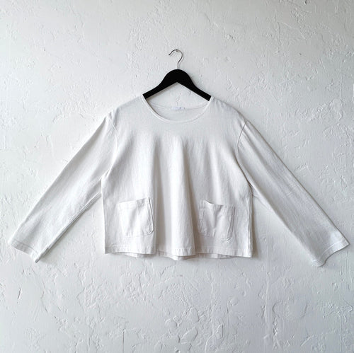 White long-sleeve crop top on a hanger against a white wall