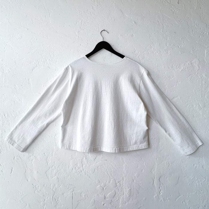 White long-sleeve shirt on a hanger against a white wall