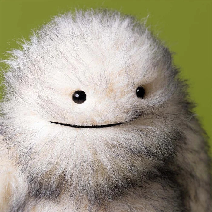 Close-up of a fluffy white creature with black eyes against a green background