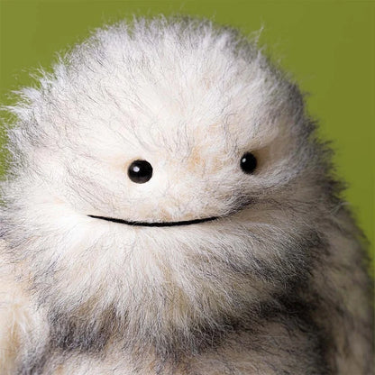 Close-up of a fluffy white creature with black eyes against a green background