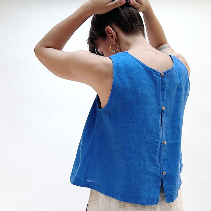 A close up shot of a person in a bright cobalt blue linen tank as seen from behind with her hands on her head