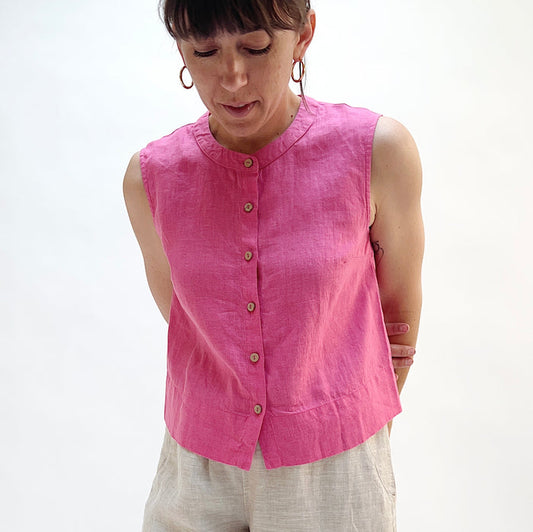 Woman wearing a pink sleeveless linen top with buttons on a white background.