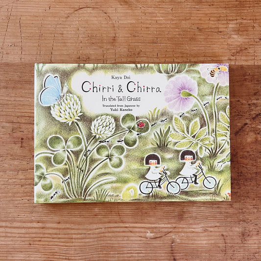 Cover of 'Chirri & Chirra: In the Tall Grass' featuring illustrations of two children on bicycles, surrounded by grass, flowers, and a butterfly.