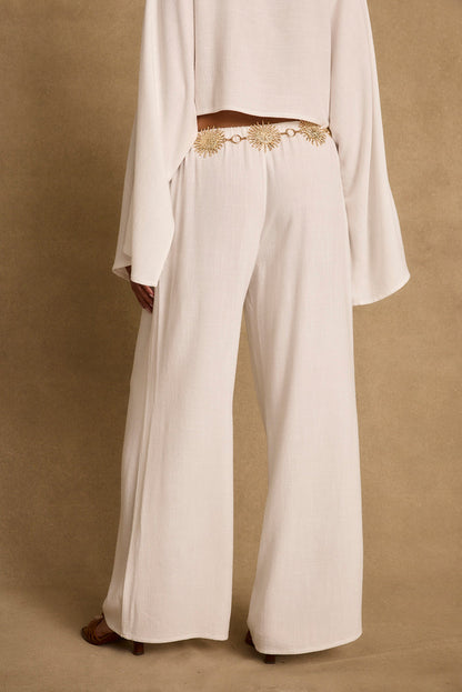 Cropped view of white linen wide-leg pants styled with a gold sunburst chain belt.