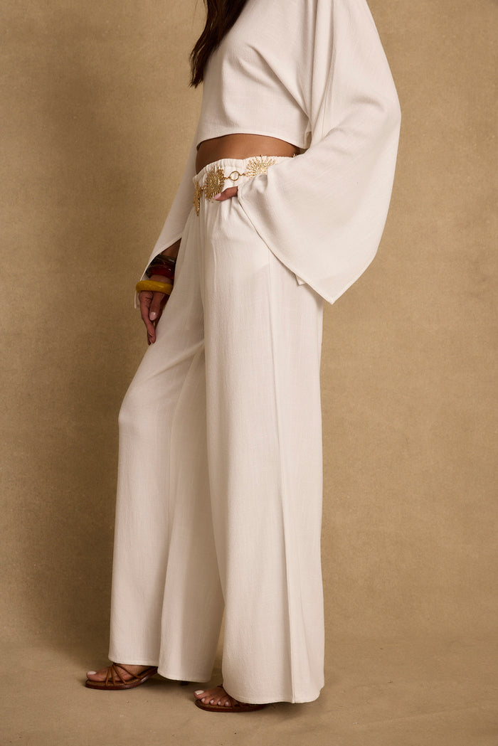 Side view of white linen wide leg pants styled with a gold chain belt and matching crop top.