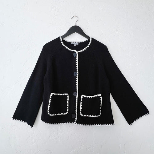 Black knit jacket with white trim on a hanger against a white wall