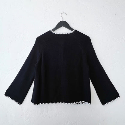 Back side of a black sweater with white trim on a hanger against a white wall.