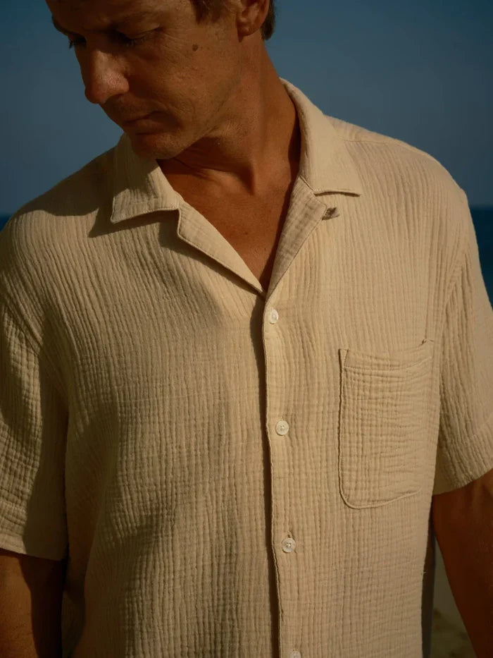 A man looking down at the ground wearing a oat colored shirt