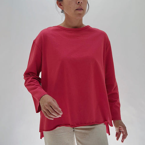 North Star Base Cotton Jersey Beach Tee in Cayenne — front view showing the oversized boxy fit, crew neckline, long sleeves, and curved hem with side slits in cayenne red, worn with cream trousers on a white background