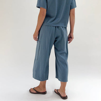 Back view of model wearing Bryn Walker vitznau cotton Pasha pant, showing large patch pocket on back leg, wide cropped silhouette, elastic waistband, and dusty blue color