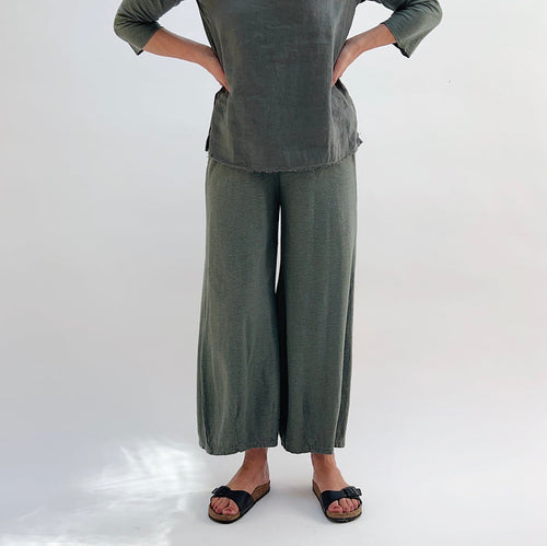 A person wearing a pair of cropped pants with darts at the hemline, made of cotton and linen blend, in a green color.