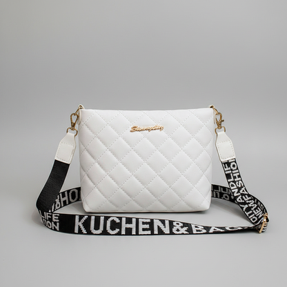 A white quilted crossbody handbag with gold-tone hardware and a black-and-white branded shoulder strap, photographed on a light gray studio background.