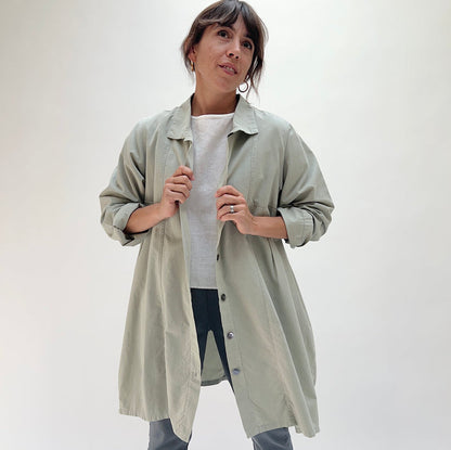 Model holding open Eleven Stitch artichoke darted coat, showing button-front closure, point collar, and relaxed A-line silhouette layered over a white tee