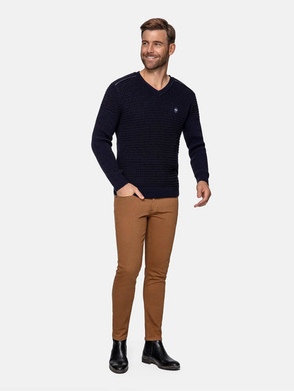 Man wearing slim-fit camel brown jeans paired with navy V-neck sweater and black boots – Wam Denim.