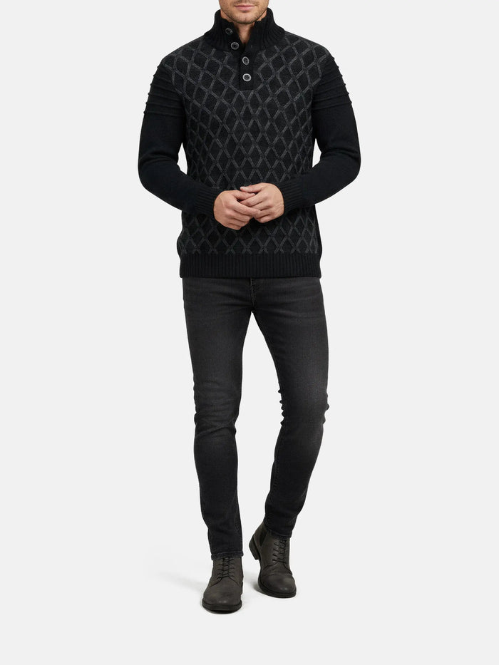 Full-body view of a man wearing an anthracite textured knit sweater with dark jeans.