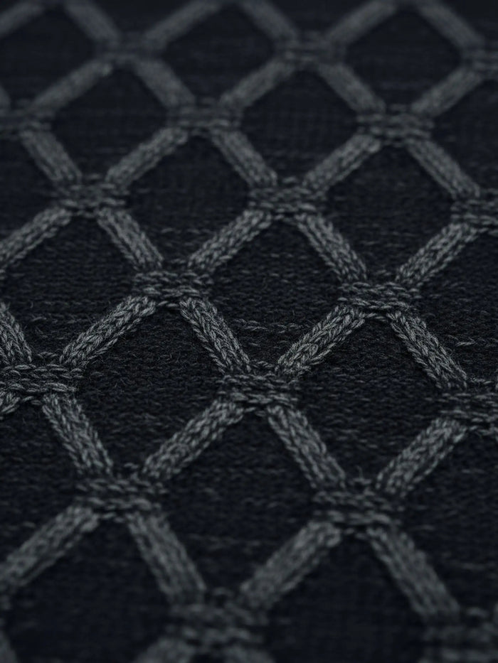 Close-up of anthracite knit sweater fabric featuring a raised geometric diamond pattern.