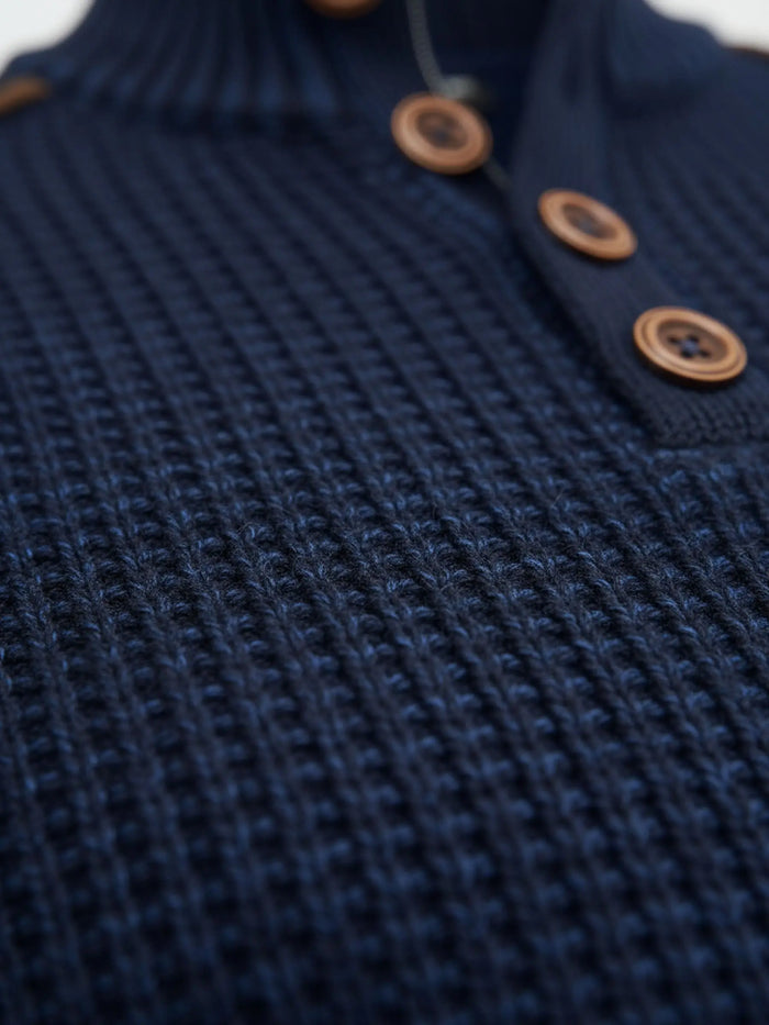 Close-up of indigo navy knit sweater fabric showing thick textured waffle pattern.