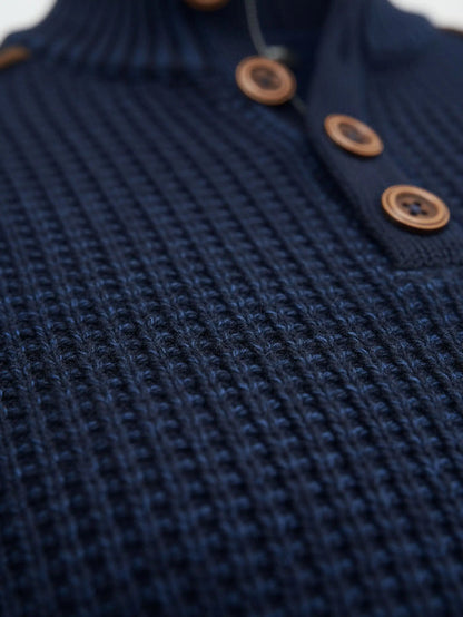 Close-up of indigo navy knit sweater fabric showing thick textured waffle pattern.