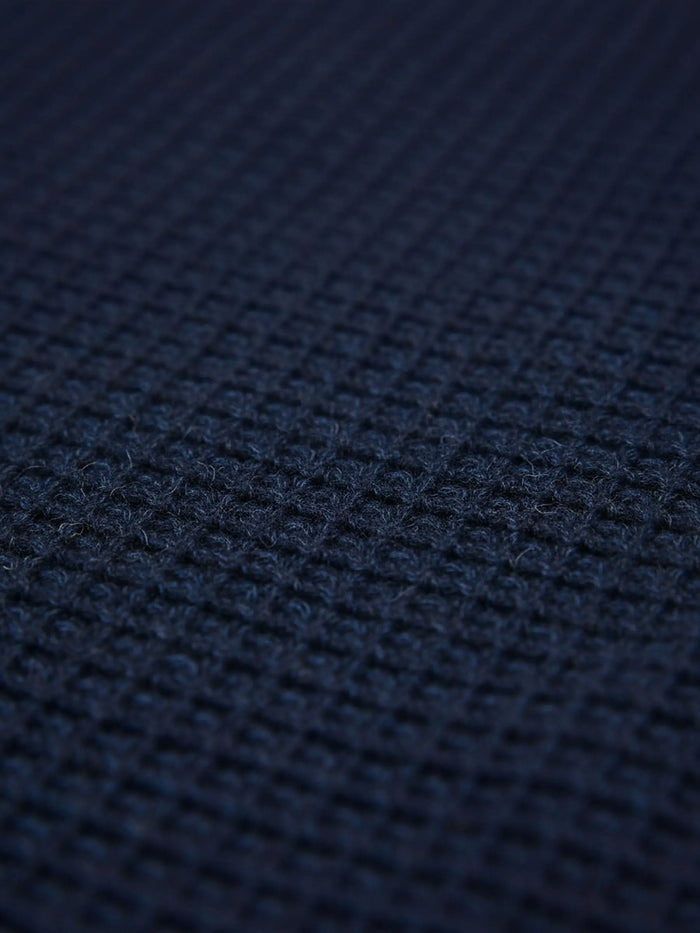 Close-up of indigo navy knit fabric showing dense textured waffle pattern.