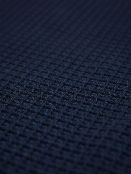 Close-up of indigo navy knit fabric showing dense textured waffle pattern.