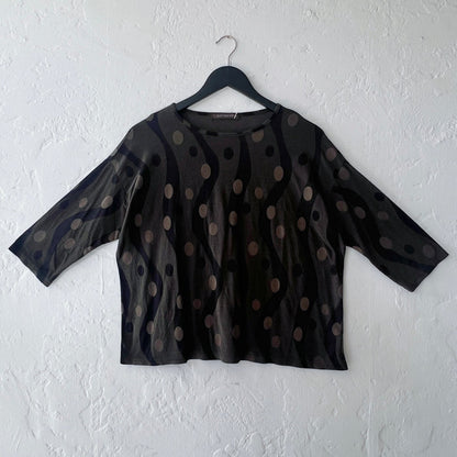 Dark green polka dot blouse on a hanger against a white wall