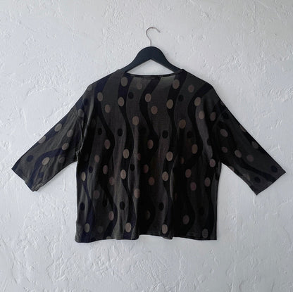 Dark green polka dot blouse on a hanger against a white wall
