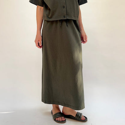 Person wearing a long olive green skirt with a plain background