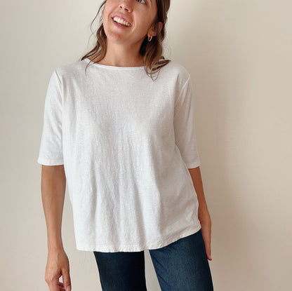 A person standing against a white background, wearing a white elbow sleeve top and blue jeans.