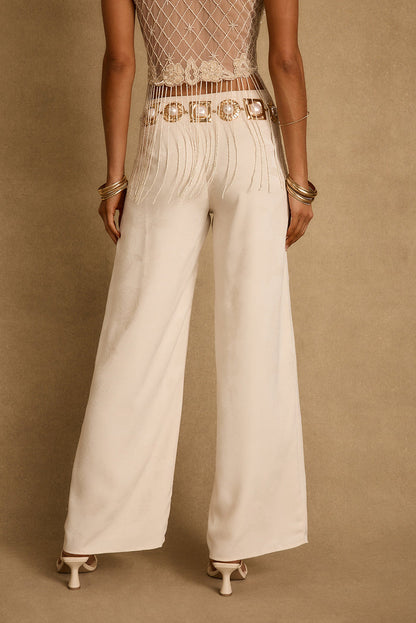 Back view of ivory jacquard wide-leg trousers styled with pearl belt and gold bangles.