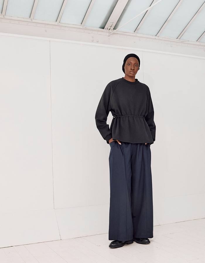 Model wearing navy boyfriend fit flared pants paired with a black long-sleeve top, styled in a minimalist setting emphasizing clean lines and understated elegance.