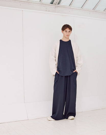 Young person wearing navy wide-leg, wrinkle-resistant pants paired with a loose navy shirt and light beige oversized jacket, standing in a minimalist white space.