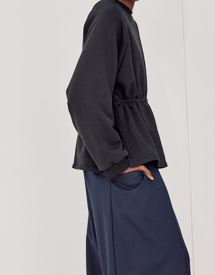 Side view of a person wearing navy boyfriend fit flared pants paired with a black long-sleeve top featuring a cinched waist, showcasing a minimalist and elegant style.