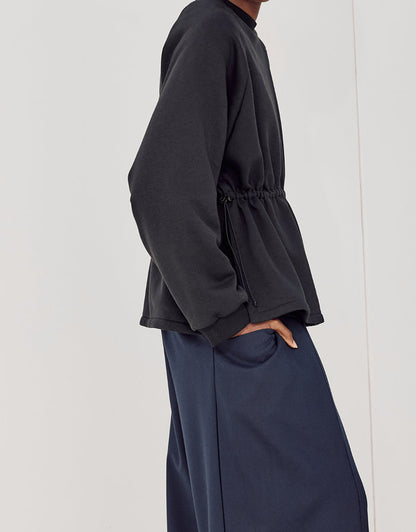 Side view of a person wearing navy boyfriend fit flared pants paired with a black long-sleeve top featuring a cinched waist, showcasing a minimalist and elegant style.