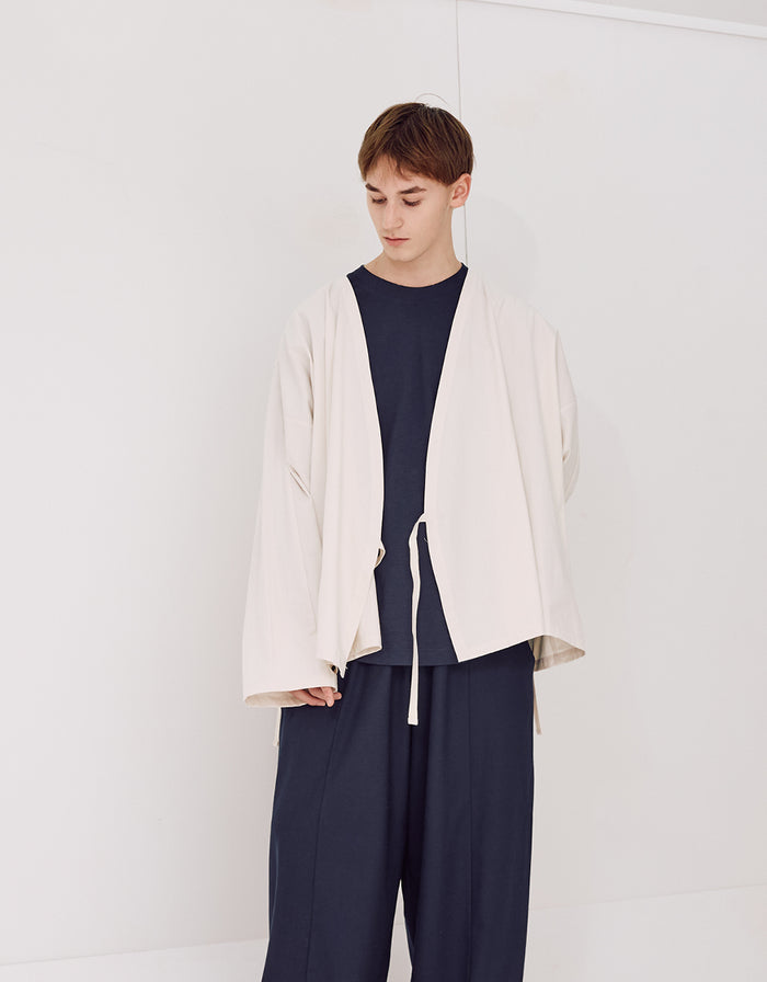 Young model wearing navy wrinkle-resistant boyfriend fit flared pants paired with a loose, light-colored minimalist jacket in a simple studio setting.