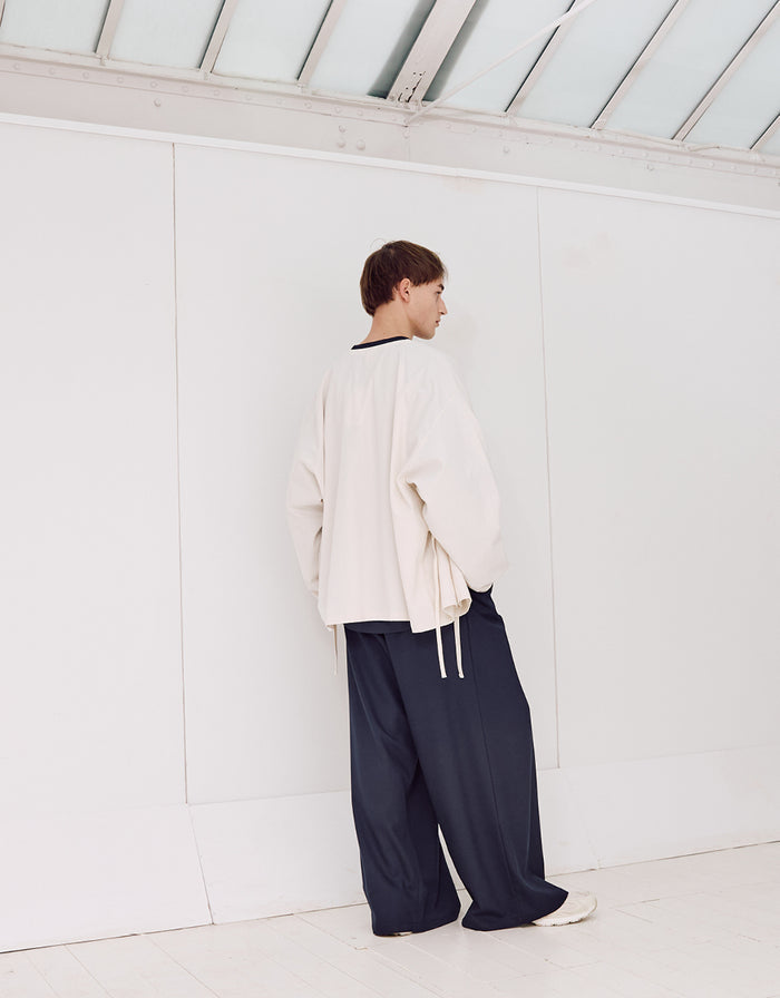 Person seen from behind wearing navy wide-leg, wrinkle-resistant pants paired with an oversized light beige top in a minimalist, bright indoor setting.