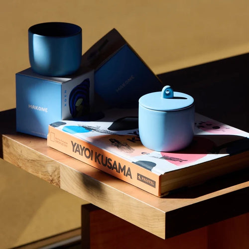 Blue ceramic vessel containing the candle on a book with a blurred background
