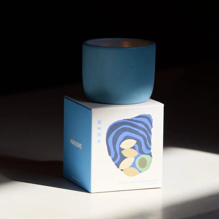 Blue candle on a white box with a blue label against a dark background