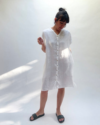 Woman wearing a white dress with buttons down the front against a white background