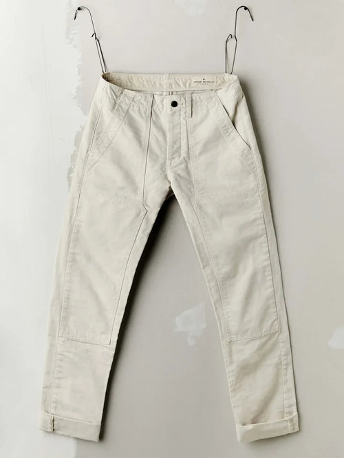 Flat lay of the Hencye Canvas Workpant in Natural showing the front waistband, belt loops, and patch pockets in natural off-white 12 oz cotton canvas, styled with workshop tools