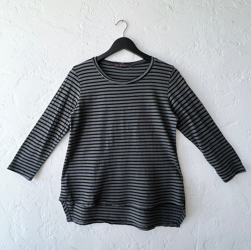 Black and gray striped long-sleeve shirt on a hanger against a white wall
