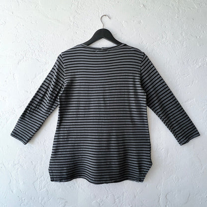 Black and gray striped shirt on a hanger against a white wall as viewed from the back