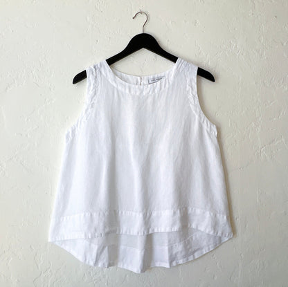 White linen high-low tank top by Cut Loose on a hanger, showing the relaxed A-line silhouette, scoop neck, and curved high-low hem